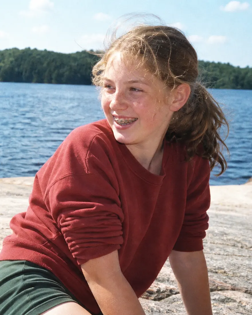 A girl smiling with braces on the granite shore of Lake of the Woods